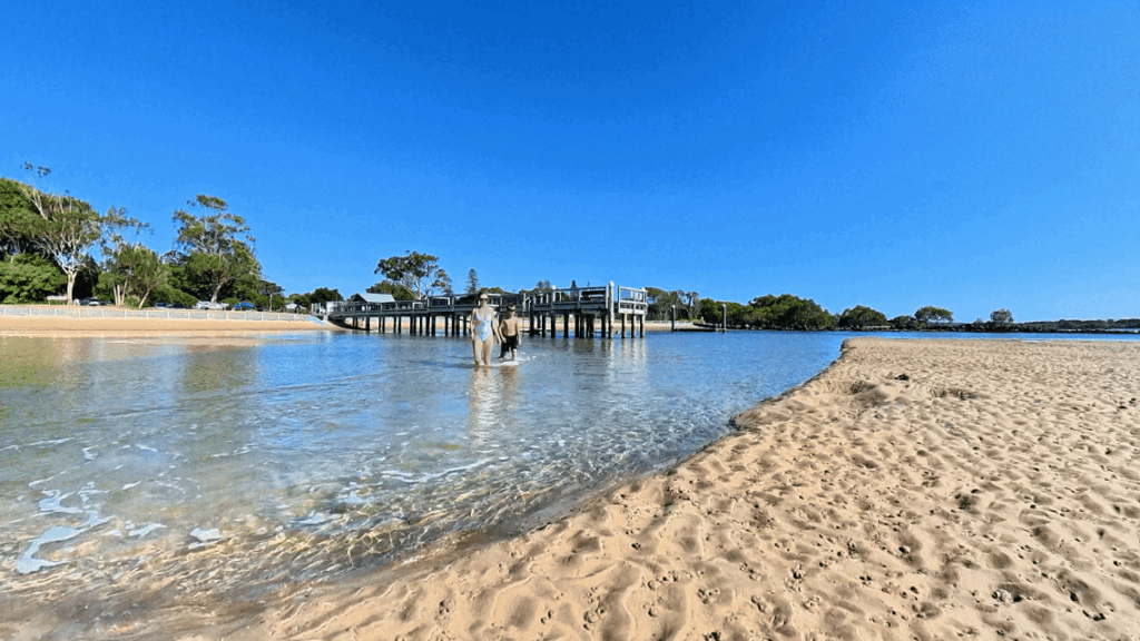 Two people walking across the sandbank beside the jetty at Urunga Lido, Mid North Coast NSW