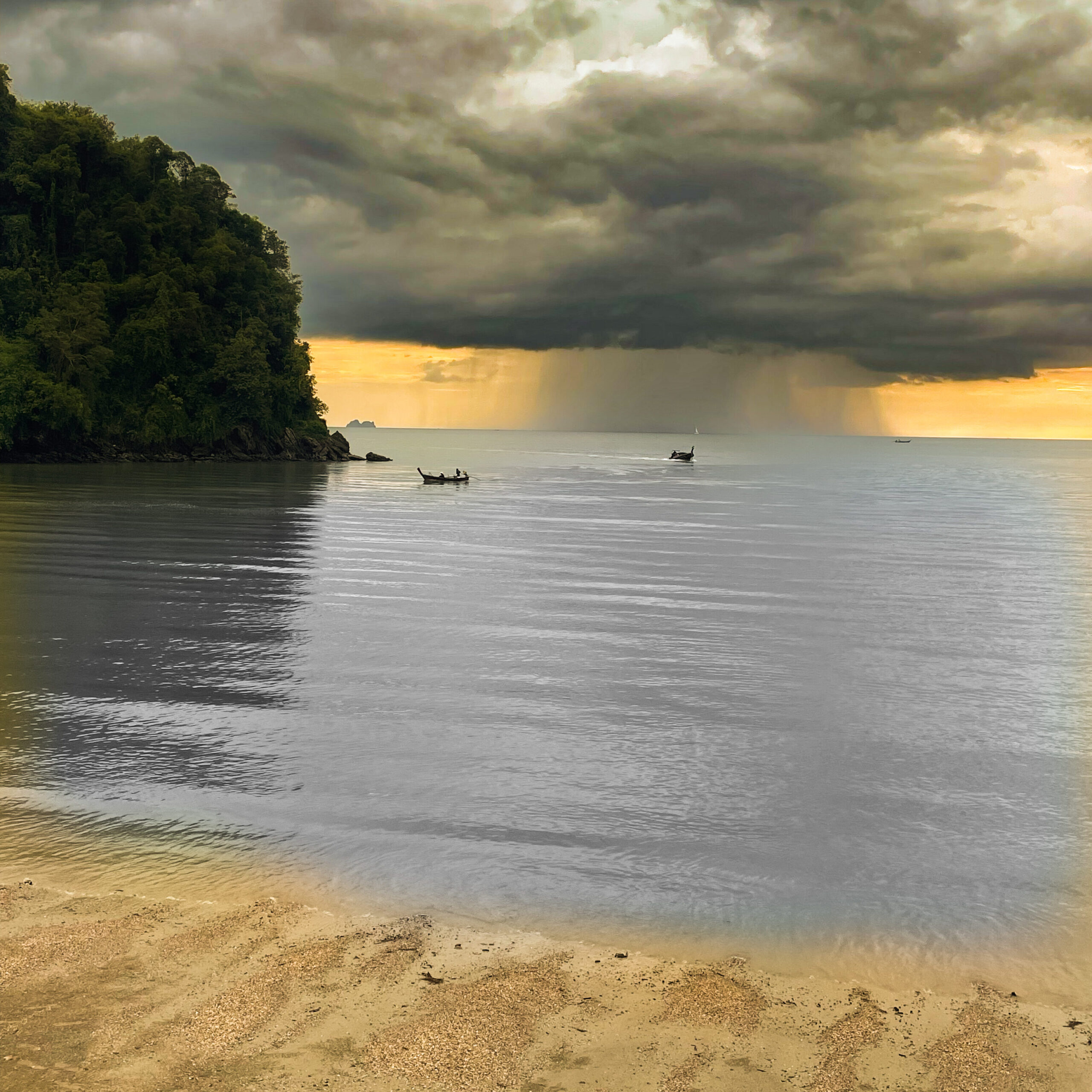 Sunset over the Andaman Sea at Ao Nang Beach Krabi Thailand with limestone cliffs, longtail boats and calm water