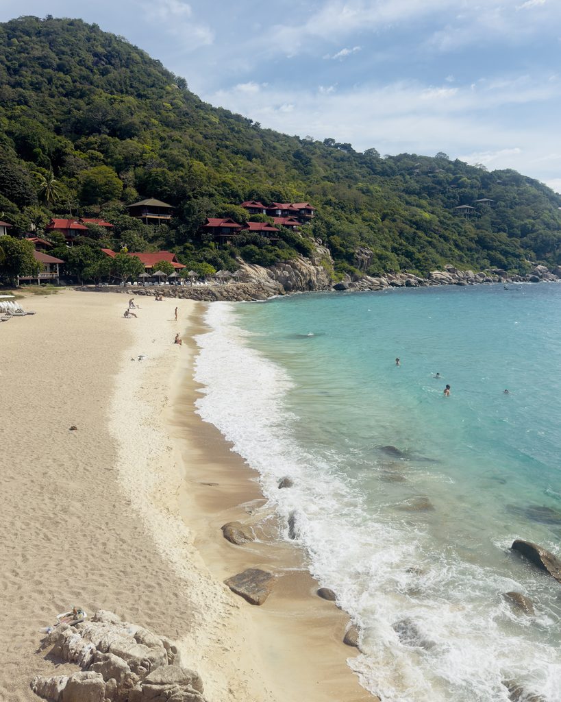 Ao Leuk Beach in Koh Tao, Thailand, with clear turquoise water, a sandy shoreline and lush green hills surrounding this popular swimming and snorkelling beach