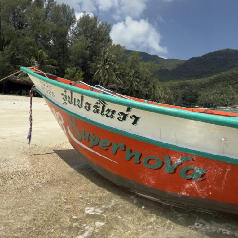 Traditional longtail boat on a sandy beach in Koh Tao, Thailand, surrounded by tropical green hills and turquoise ocean scenery