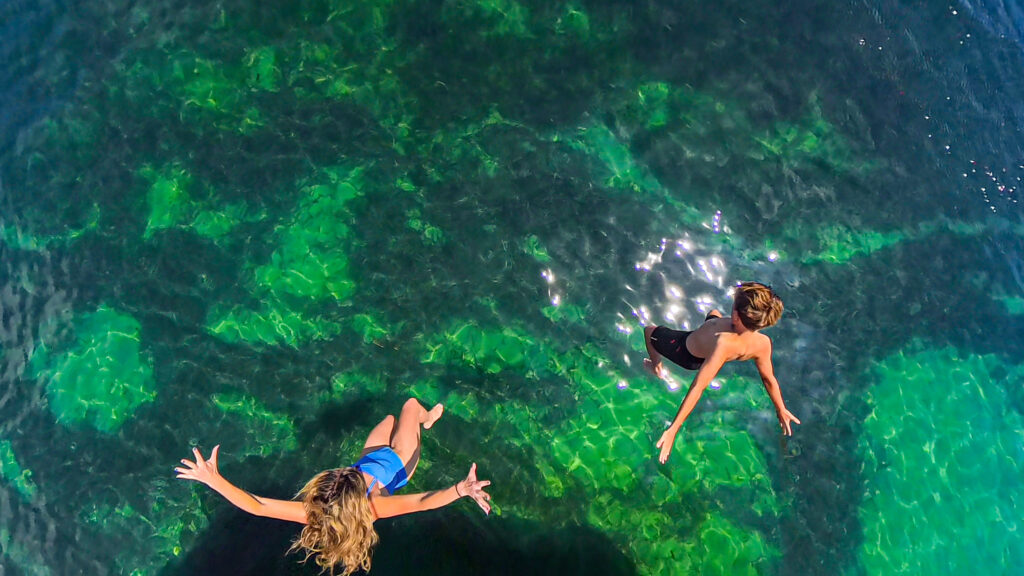 Kids jumping into the clear turquoise water from Shoal Bay Wharf in Port Stephens NSW, a fun family activity on the New South Wales coast