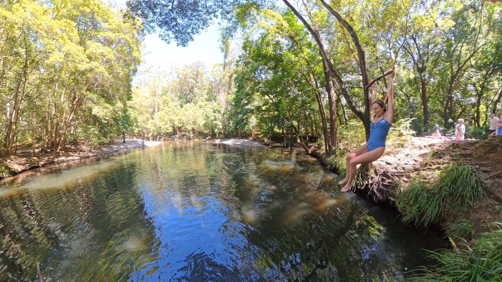 Person swinging on a rope over a freshwater swimming hole at Promised Land near Bellingen, NSW
