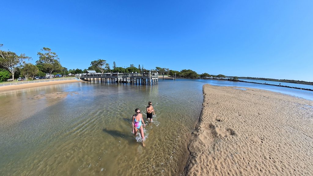 People wading through the shallow water beside the sandbank at Urunga Lido, Mid North Coast NSW